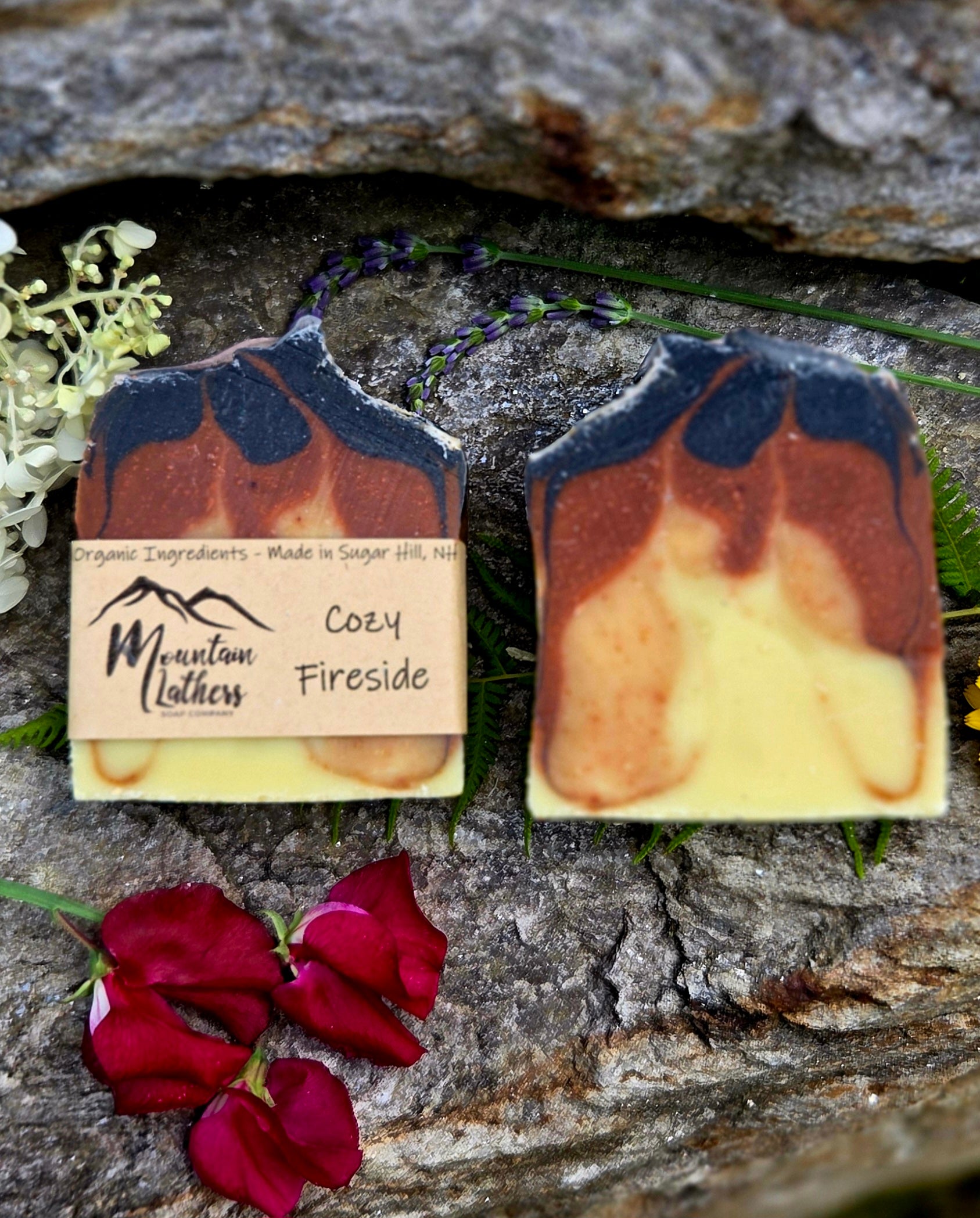 Two handmade soap bars with a marbled orange, brown, and pale yellow design, each with a kraft paper label. The label reads 'Mountain Lathers' and 'Cozy Fireside'.